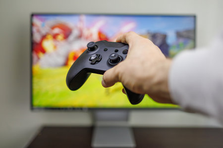 There's a gamepad in the background of the game monitor in his hands Video game gamepad in hand