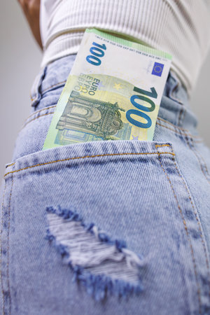 A close-up of a hundred euro bill sticking out of the back pocket of his jeans. A girl in jeans with...