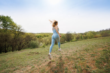 Athlete girl who runs around the park practicing. Beautiful blonde Caucasian woman in blue tight tracksuit. Blonde girl at an outdoor training sessionの写真素材