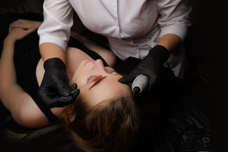 In front of a young girl stands and leaning master of permanent makeup straight he brings the eyebrows of a young girl to a beautiful look. Permanent eyebrow makeup, eyebrow tattooing with brown pigment for PMU.の写真素材