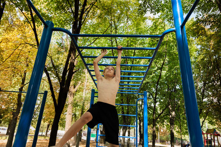 A teenager climbs a horizontal ladder with his hands above his head Athletic teenage boy in the park outdoor workout sessionの写真素材