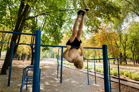 Athletic teenager hanging upside down on a crossbar. Athletic teenage boy in the park outdoor...