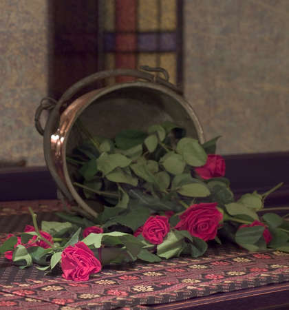 Red roses falling fron copper vase in front of old mirror glassの写真素材
