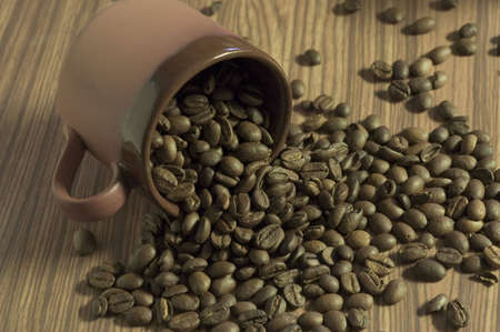 Brown cup filled with coffee beans against wooden backgroundの写真素材