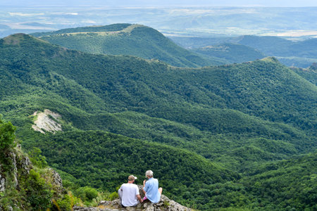 Senior couple sitting on the top of a mountain and looking at the valleyの写真素材
