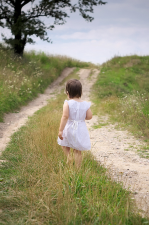 little girl walks barefoot along the roadwhite dress and barefootroad sandの写真素材