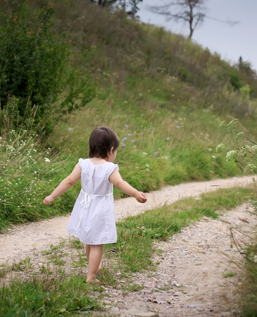 a child walks barefoot on the sandy roadwhite dress and barefootroad sandの写真素材