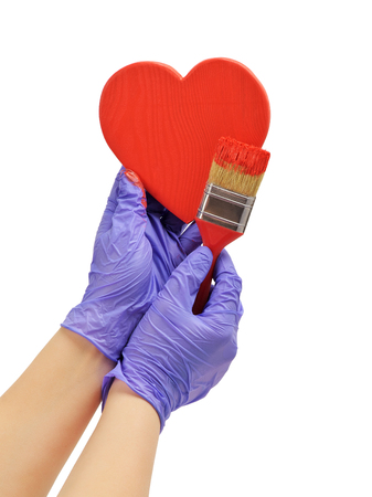 hand paints the heart with a brush
hand paint in red wooden heart
hand in blue glove holds a red brushの写真素材