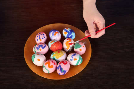 girl paints Easter eggs. hand, brush and paint on the table. preparation for Easter. wooden table.の写真素材
