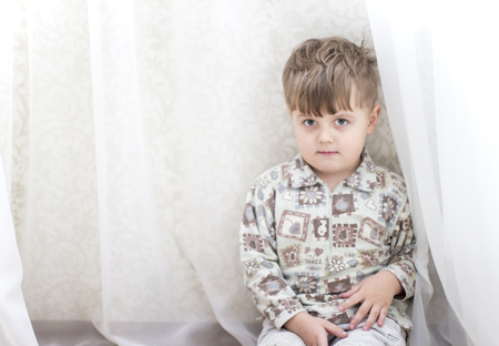 Little boy near a white curtains. Emotions. Emotions of a little boyの写真素材