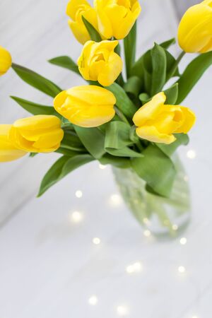 Bouquet of yellow tulips and garlands in a vase on a white wooden board backgroundの写真素材