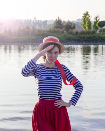 Girl in a straw hat near the water. Girl in a red skirt and a sailor suitの写真素材