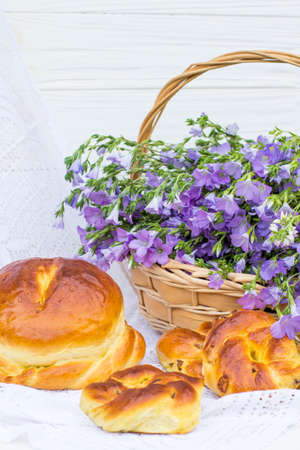 Delicious pastries (bread and rolls with raisins) and bouquet linen in wicker basketの写真素材
