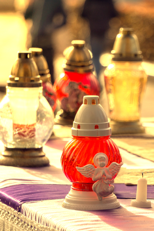 Colorful, vivid red yellow catholic lighting candles in lanterns decorated with beautiful angel are placed on draped table. All Saints' Day holiday.の写真素材