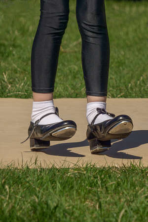 Legs and feet of young girl in black tap shoes, white socks and black tights. Dancing tap dance...