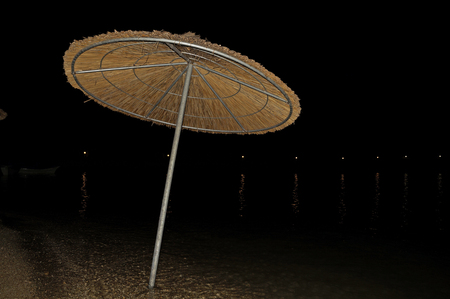 Beach umbrella stands alone at night in the water on a sandy beachの写真素材