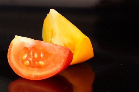 Ripe pieces of yellow and red tomatoes are isolated on a black backgroundの写真素材