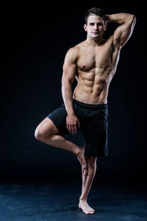 Muscular man balancing on the one leg feeling relaxed on dark backgroundの写真素材