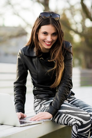 Girl works on laptop sitting on a bench in the parkの写真素材