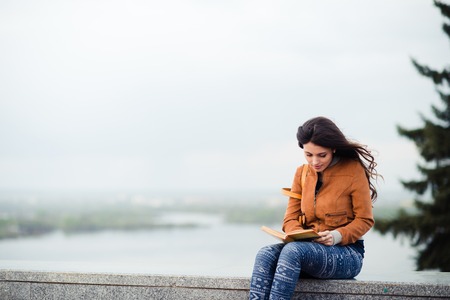 Beautiful outdoors portrait of a woman with a bookの写真素材