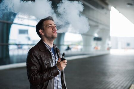 Young traveller man smoking an electronic cigarette outdoor near the airport terminal.の写真素材