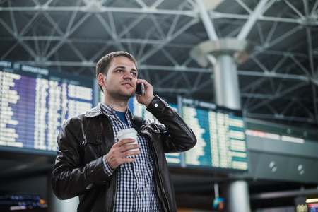 Cheerful man on the mobile phone in hall station in front of Board schedules.の写真素材