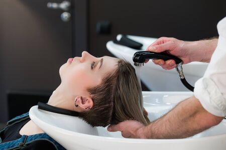 Young teenager girl in hairdressing salon washing hair by male hairdresser's handsの写真素材