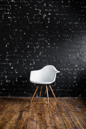 White chair standing in room on brown wooden floor over black brick wall.の写真素材