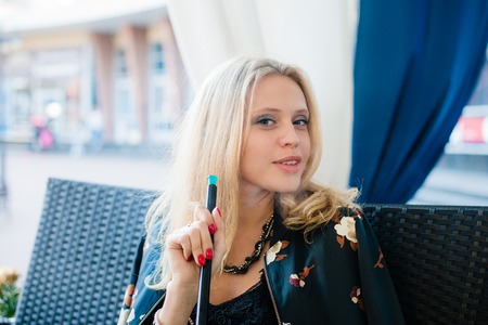 Beautiful young blonde woman smoking hookah at outdoors cafe.の写真素材