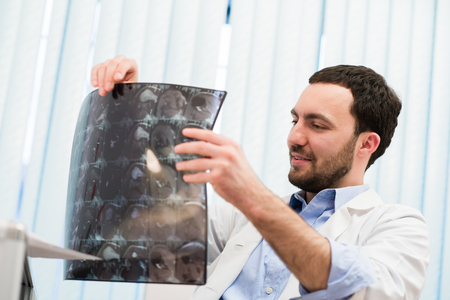 Portrait of a handsome caucasian male radiologist holding x-ray while sitting at his office.の写真素材