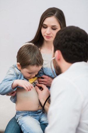 Pediatrician doctor examining kid boy. Mother holding babyの写真素材