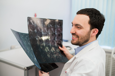 Portrait of a happy caucasian male radiologist holding x-ray while sitting at his office.の写真素材
