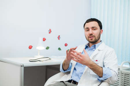 Cheerful doctor talking and looking into the camera. Doctor talking with the patient while sitting at a table in the hospital.の写真素材