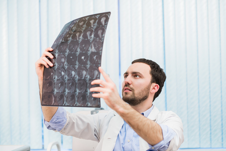 Portrait of a handsome caucasian male radiologist holding x-ray while sitting at his office.の写真素材