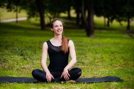 Happy, smiling, young woman resting on the grass at the park after the yoga. She is wearing dark leggingsの写真素材