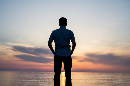 Silhouette of young man on the beach at sunset.の写真素材