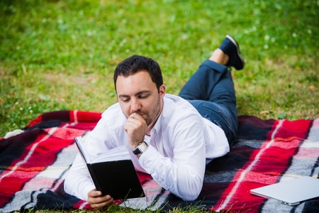 handsome young businessman reading book lying in the park.