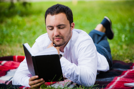 handsome young businessman reading book lying in the park.の写真素材