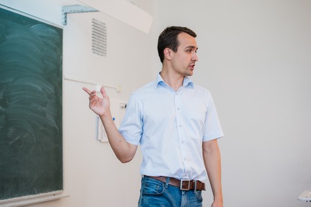 Young teacher near chalkboard in school classroom talking to class.の写真素材