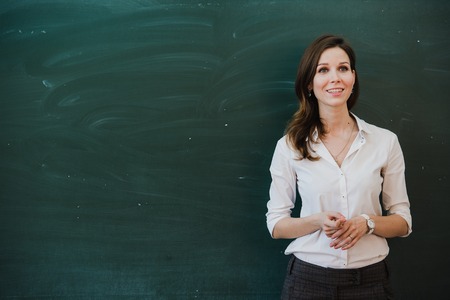 Closeup of young female teacher against chalkboard in class.の写真素材