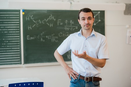Young teacher near chalkboard in school classroom talking to class.の写真素材