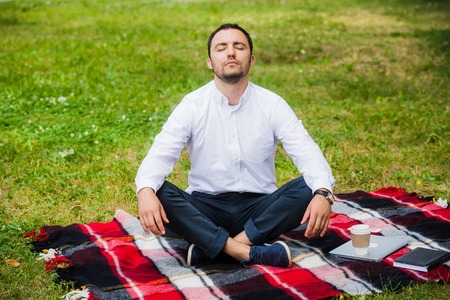 Man businessman meditating outdoors in lotus pose.の写真素材
