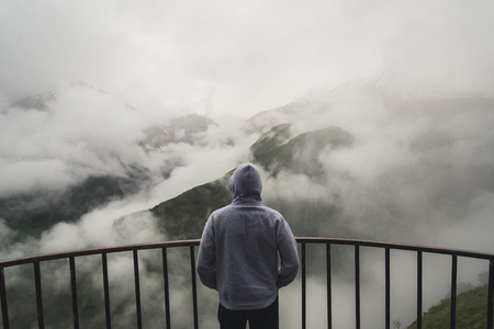 View from behind of a man standing at view point looking to beautiful landscape of foggy mountains in the distance.の写真素材
