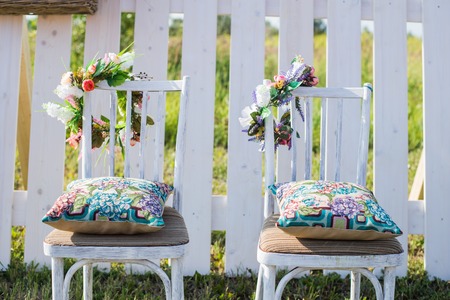 Two vintage white chairs, colorful velvet pillow and fence palisade on background decorated with flowers in boho style. Soft evening lightの写真素材