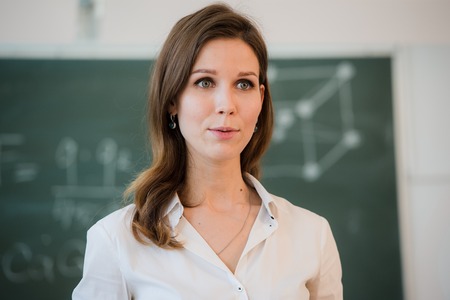 Portrait of happy teacher standing in front of black board.の写真素材