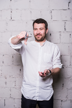 Portrait of young beautiful hairdresser man wearing white shirt with scissors ongrey brick wall.の写真素材