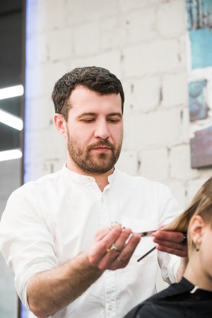 Male hairdresser making a haircut for a client in professional hairdressing salon.