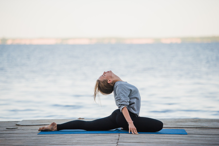 Pretty woman practicing yoga at a lake.の写真素材
