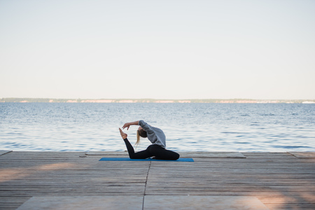 Pretty woman practicing yoga at a lake.の写真素材