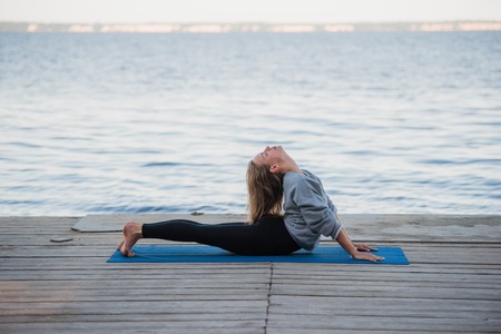 Woman doing stretching yoga exercises in the morning at the sea or lake.の写真素材